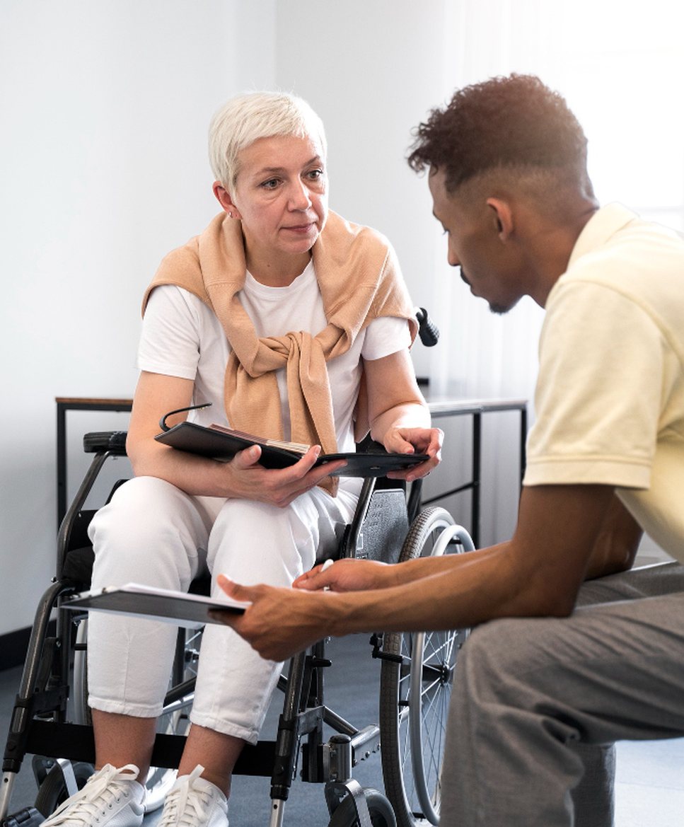 A caregiver kneeling to talk with a client in a wheelchair at eye level